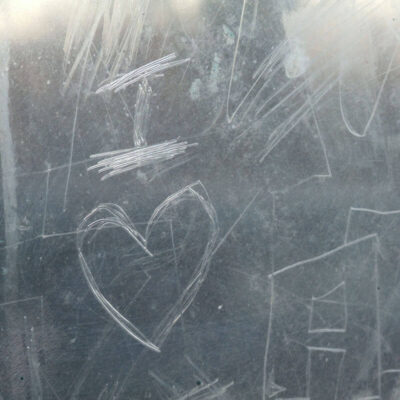 Close up image of etching on glass. Drawings of a heart and letters. The layer of film can be peeled to remove graffiti.